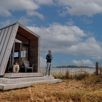 Man staat voor het Zuiderkrib Dijkhuisje met dijk en water in Kraggenburg, Flevoland